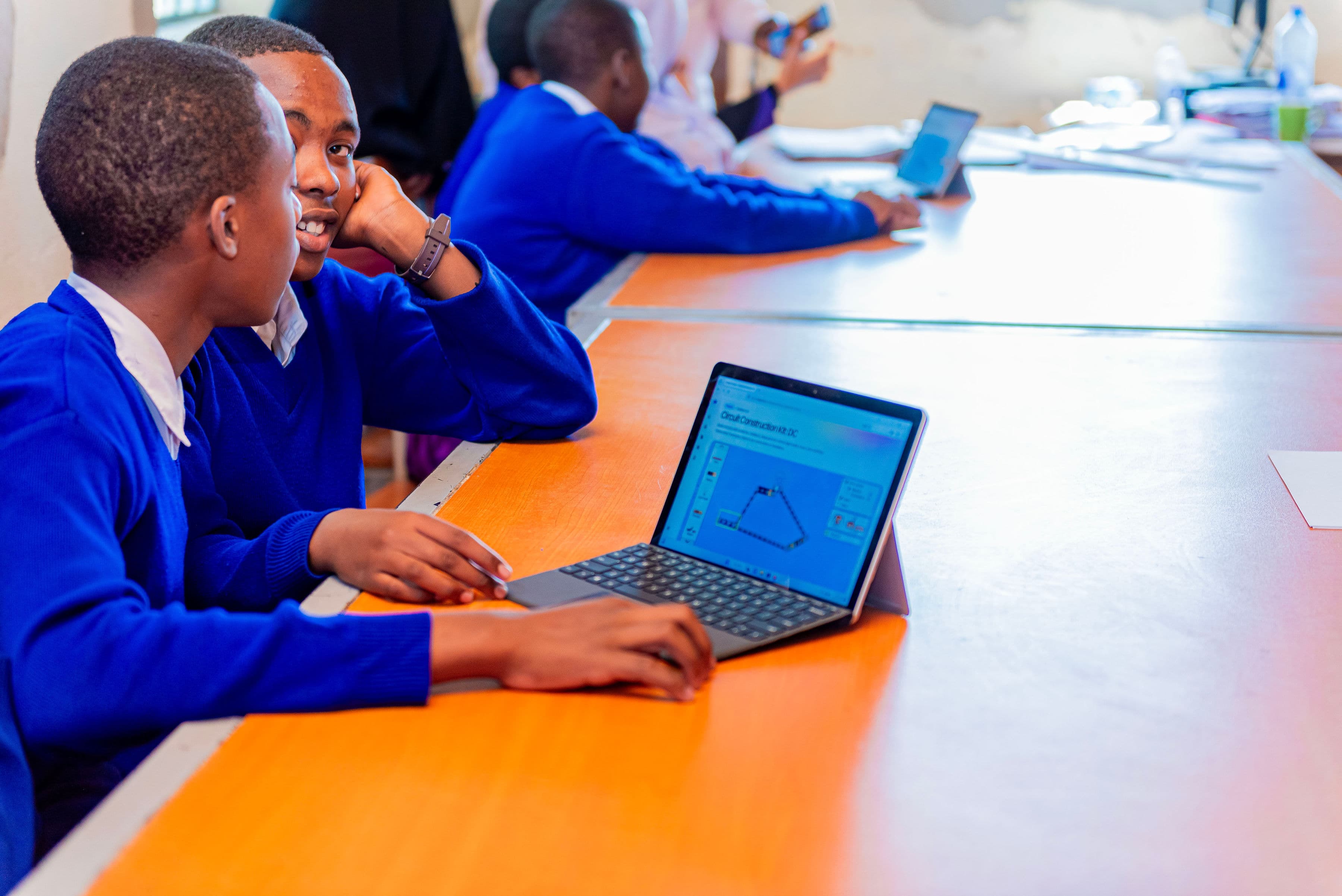 Students in blue uniforms studying together at a laptop